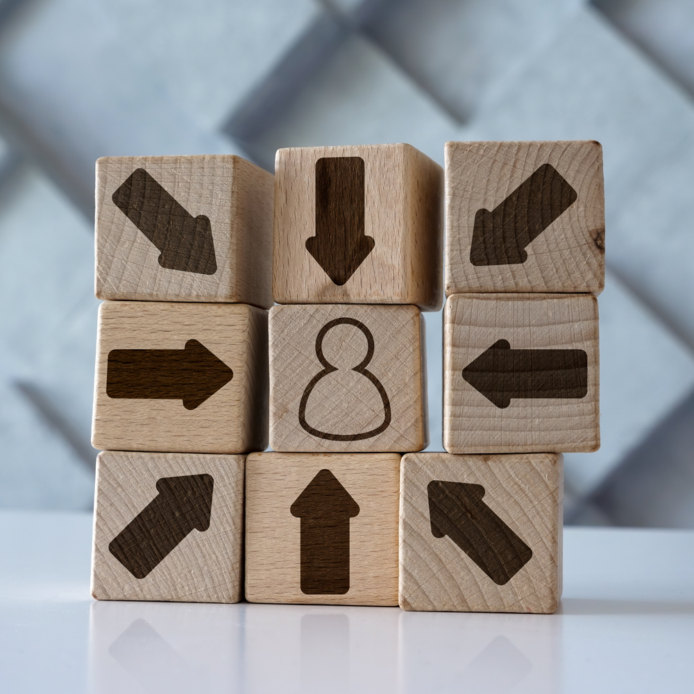 9 wooden blocks stacked in rows of three. All outer blocks have an arrow pointing towards the middle block that has an outline of a person on it